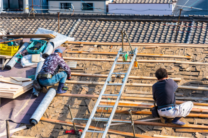 屋根瓦をはがす作業員とあらわになった家屋の屋根部分